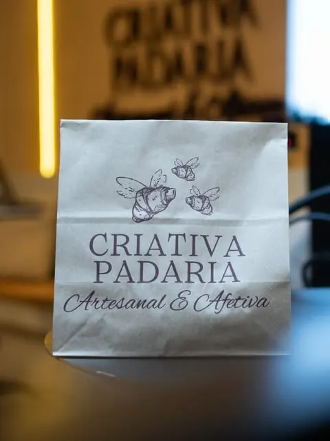 Saco de papel da Criativa com o logo carimbado: três croissants-abelha e Artesanal & Afetiva