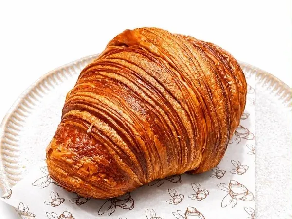 Croissant da casa, folhado e dourado, sobre o papel estampado da Criativa